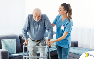 A professional caregiver helps an older man walk with a walker, showing how having a caregiver help a loved one stay mobile safely can help avoid hospital readmissions.