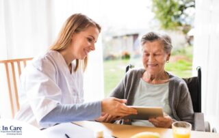 A professional caregiver smiles as she helps a happy senior client with her tablet, showing that she is managing caregiving stress well.