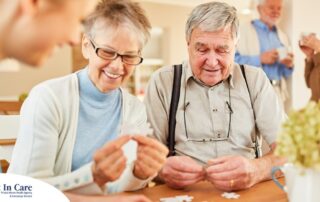An older couple works on a puzzle with a caregiver, representing the kind of activity that helps those with dementia and also representing Alzheimer’s and Brain Awareness Month.