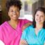 2 caregivers smile representing the good attitude that can allow home care professionals to collaborate.