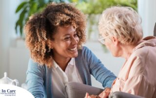 A caregiver smiles at an older client in a chair, representing the joy that can come from a healthy work-life balance.