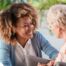A caregiver smiles at an older client in a chair, representing the joy that can come from a healthy work-life balance.