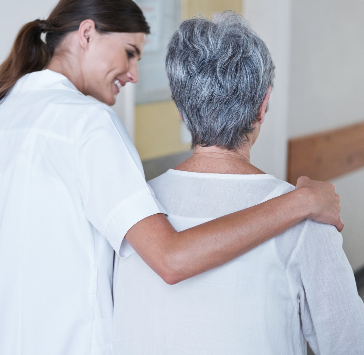 A caregiver gently supports a senior woman while walking down a hospital hallway, reflecting compassionate Hospital Companions in Lakewood Ranch.