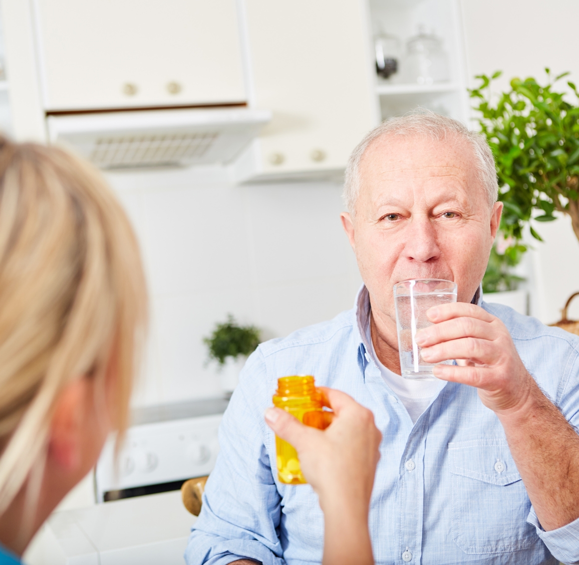 A senior man takes medication with a glass of water while being assisted by a caregiver, illustrating reliable Medication Reminders in Lakewood Ranch.