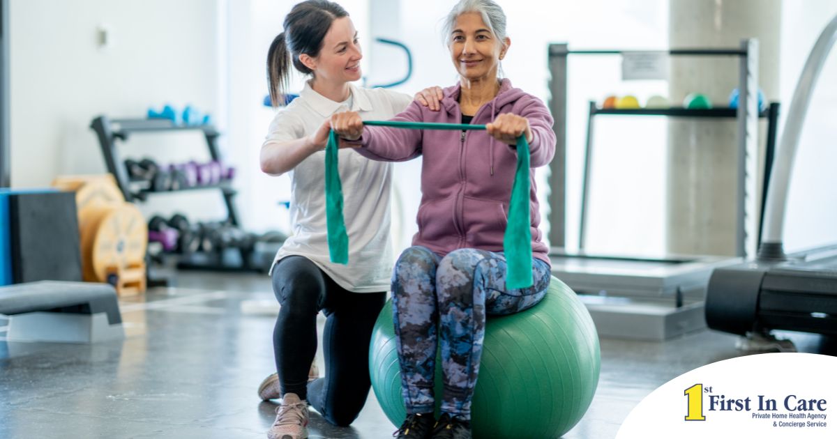A care provider helps an older woman exercise with a resistance band and an exercise ball, representing how exercise can help with senior fall prevention.