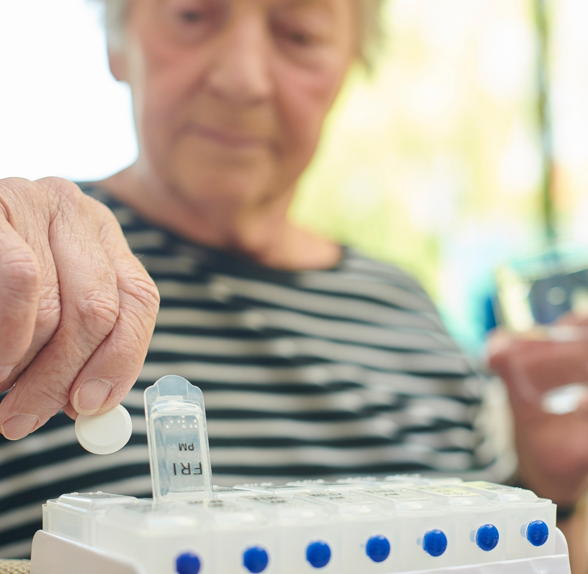 Senior placing medication into a weekly pill organizer as part of daily Medication Reminders in Manatee County